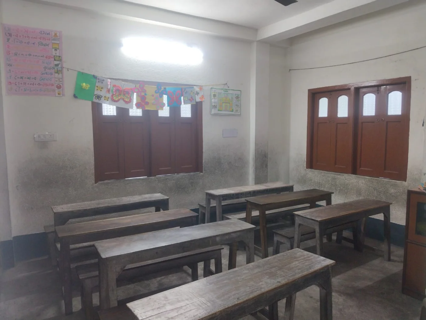 Classroom with wooden benches, decorated walls and natural light at Swapno Chhoya